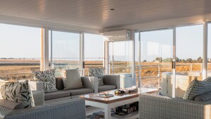 A sunlit room with a large window, wicker furniture, and a view of a field. - Chobe Princess By Mantis (Kasika)