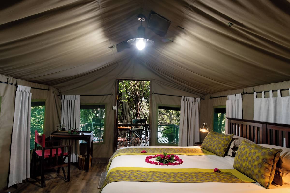 A tented accommodation with a bed, a table, and chairs.