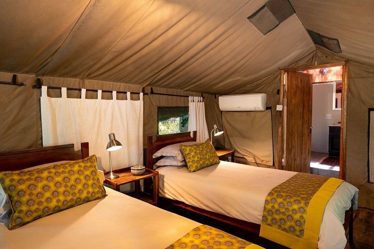 A tent with two beds, a window, and an air conditioning unit.