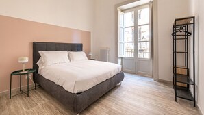 Ein Schlafzimmer mit einem Bett, einem Nachttisch, einem Heizkörper, einem Fenster und einem Wandregal.
