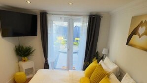 Ett hotellrum med en stor säng, en platt-TV som är monterad på väggen, en liten krukväxt och utsikt över omgivningarna genom en glasdörr.