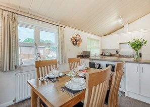 Un coin repas avec une table dressée pour quatre personnes, une cuisine équipée d’appareils modernes et une vue sur l’extérieur.