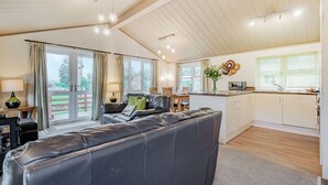 Un salón amplio con un sofá de cuero grande, una mesa de comedor con sillas, una zona de cocina y un ventanal corredero que da a una terraza exterior.
