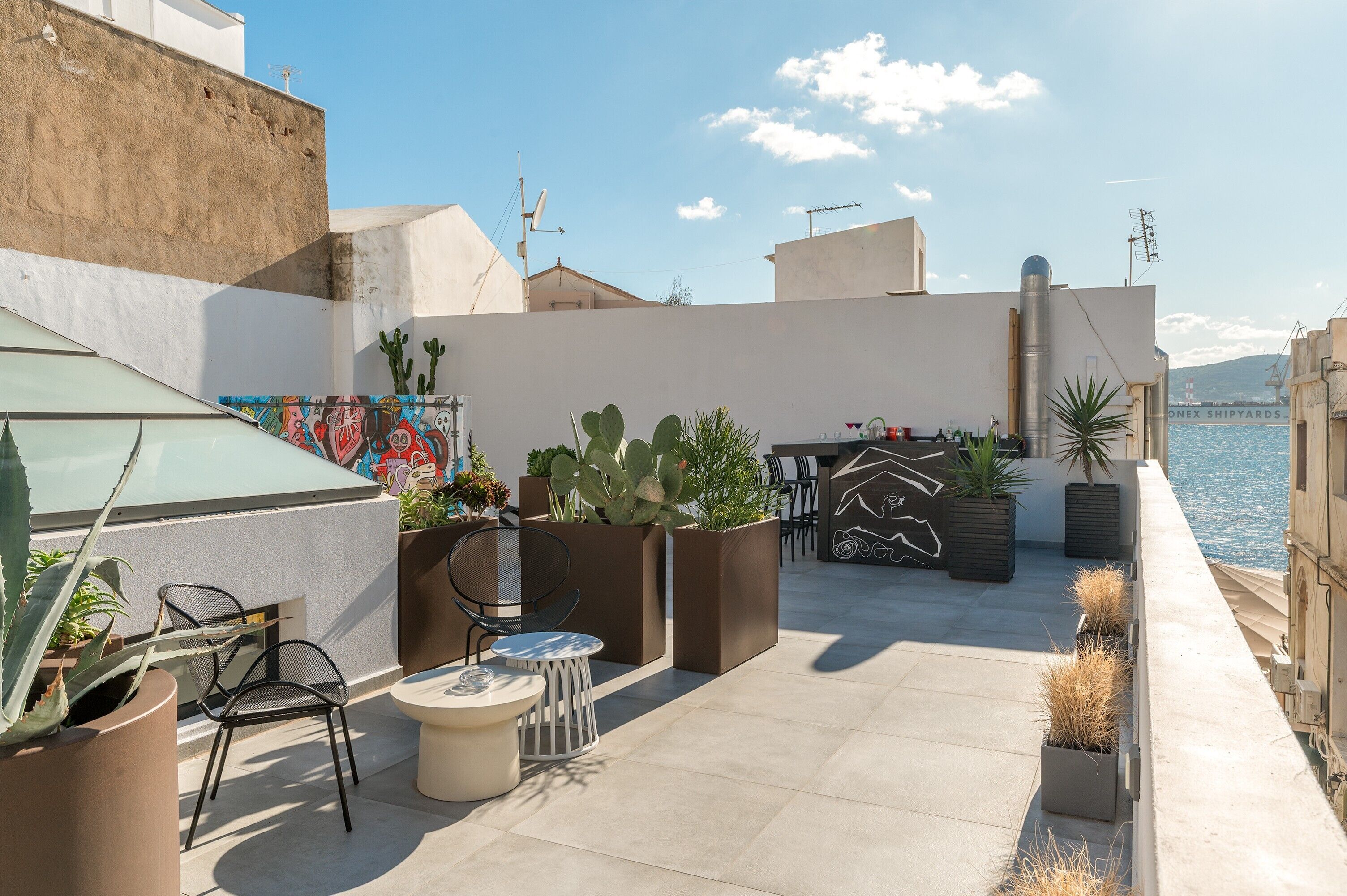 Eine Dachterrasse mit Sitzgelegenheiten im Freien, Topfpflanzen und Blick auf das Meer.