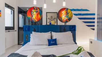 A modern bedroom with a blue headboard, white bedding, and two abstract paintings above the bed.