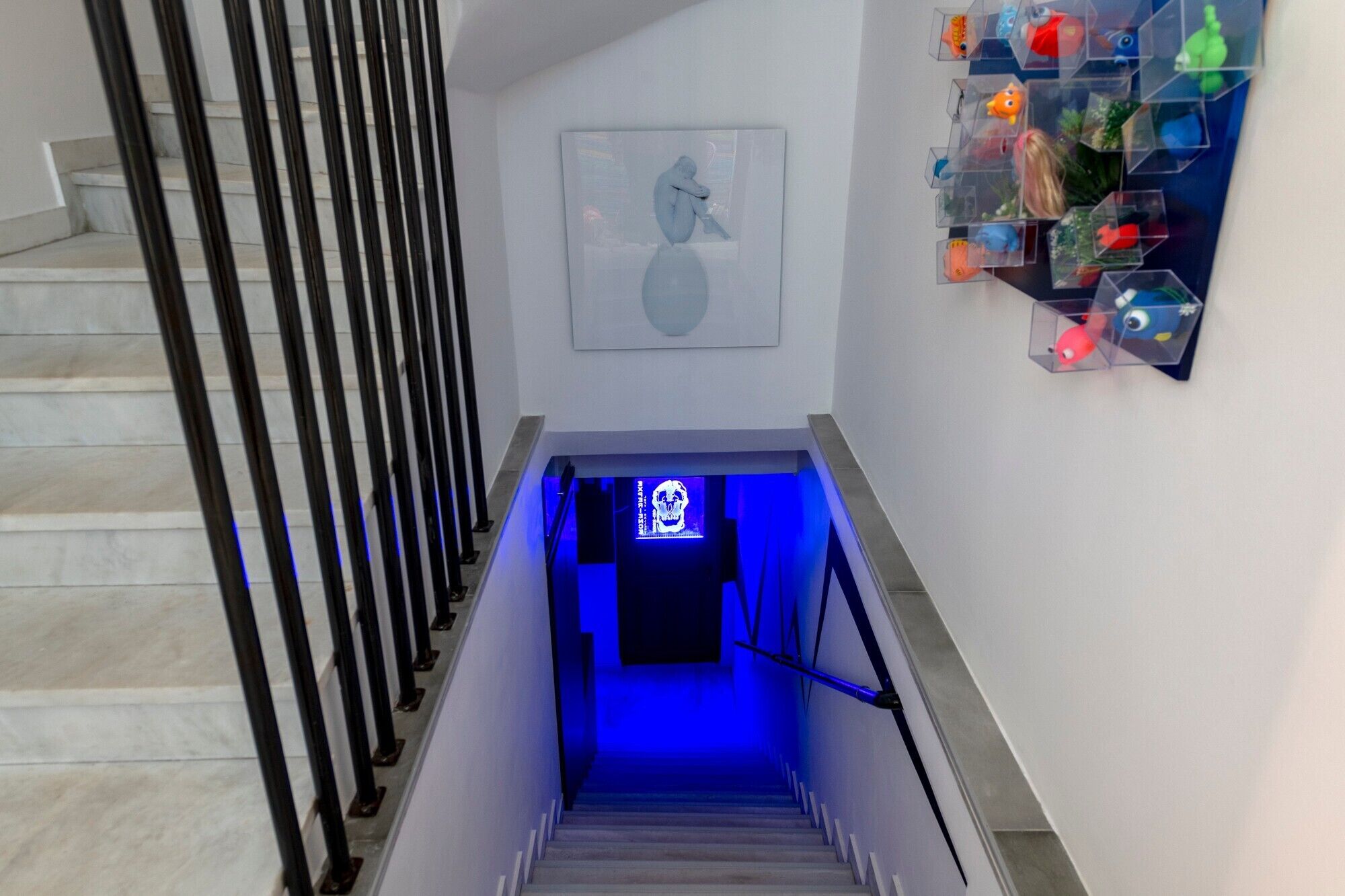 Una escalera con una pared iluminada en azul, una obra de arte enmarcada y un estante con objetos coloridos.