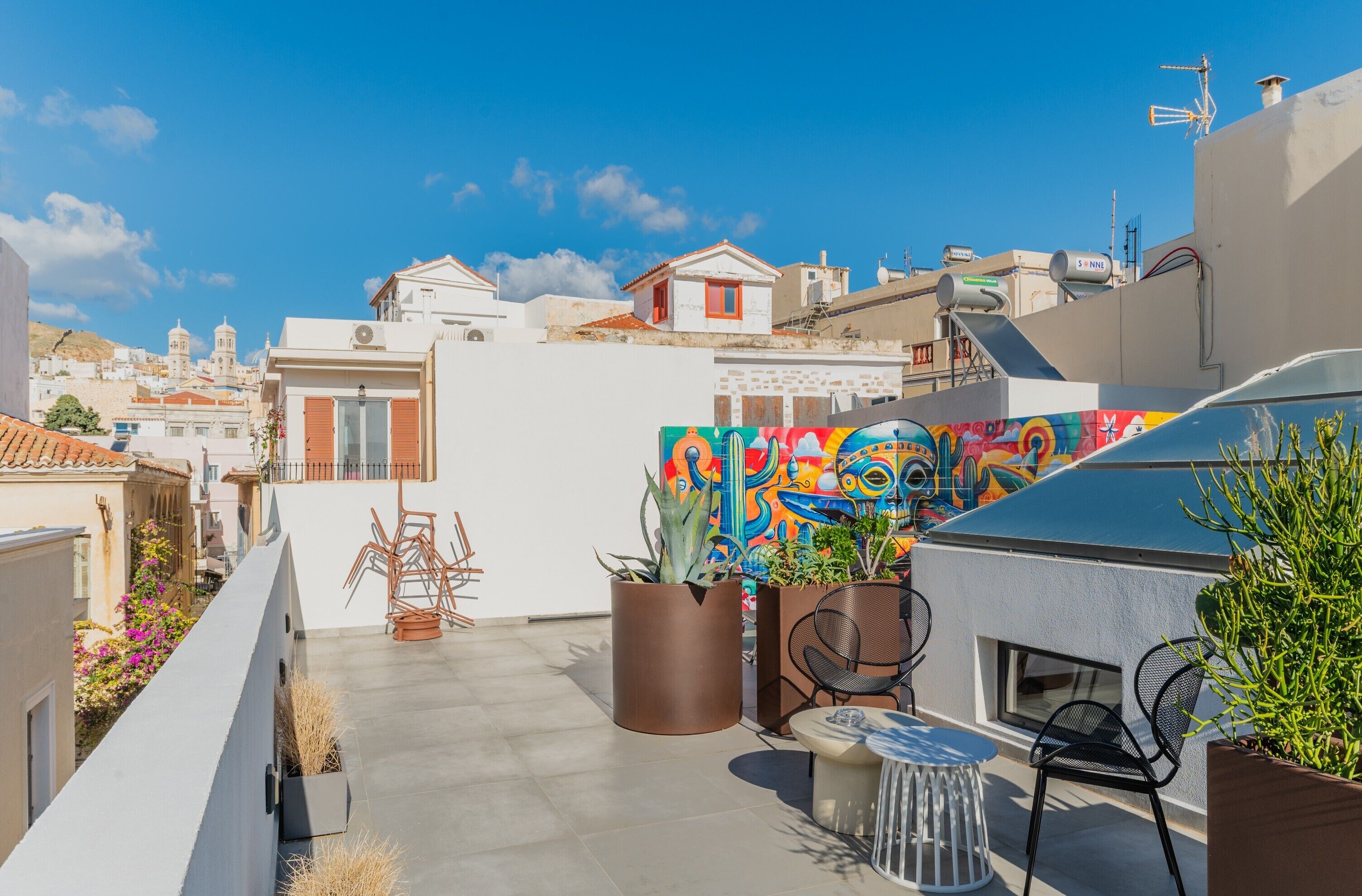 A rooftop terrace with potted plants, a table, and chairs.