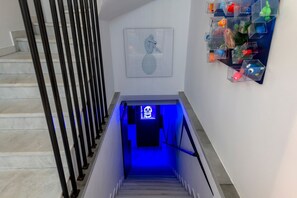 A staircase with a blue-lit wall, a framed artwork, and a shelf with colorful objects. - Apartment 'Pop Loft Gallery' with Sea View, Wi-Fi and Air Conditioning (Ermoupoli)