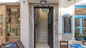 A narrow staircase leading to a building entrance with a sign listing amenities. - Apartment 'Pop Loft Gallery' with Sea View, Wi-Fi and Air Conditioning (Ermoupoli)