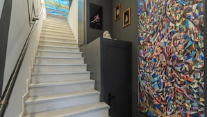 A staircase with white steps and a metal handrail, leading to a room with a large abstract painting on the wall. - Apartment 'Pop Loft Gallery' with Sea View, Wi-Fi and Air Conditioning (Ermoupoli)
