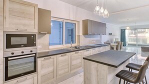 Et moderne køkken med indbyggede hårde hvidevarer, en stor køkkenø og udsigt til opholdsstuen.