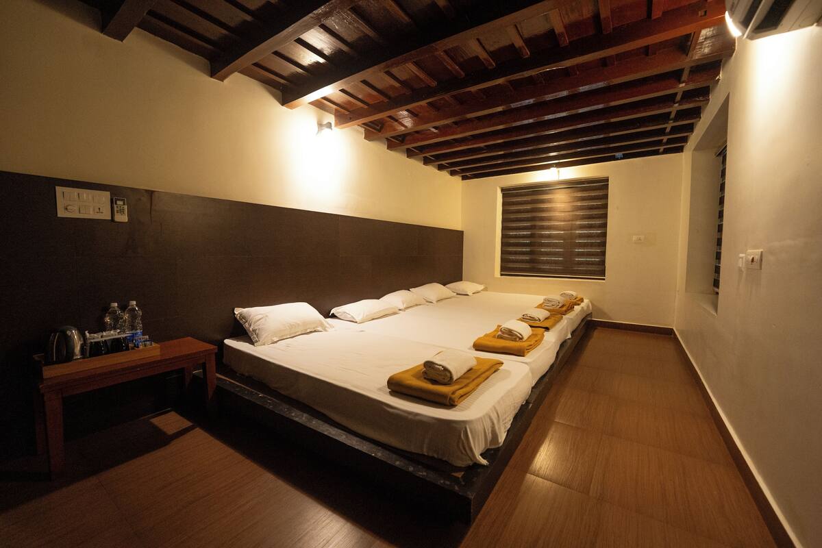 Hotelkamer met groot bed, houten hoofdbord, een bankje met toiletartikelen en een raam met zonwering.