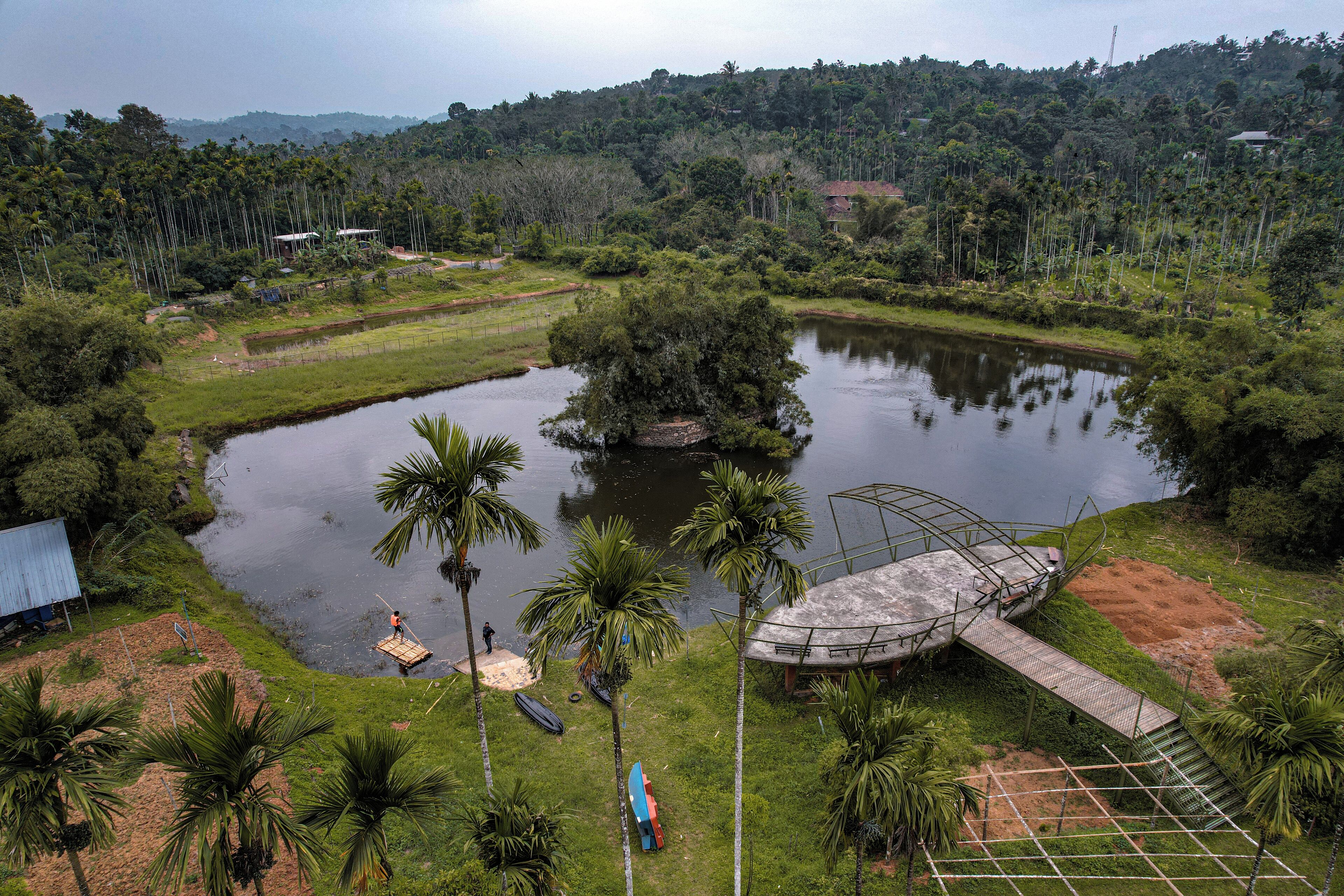 A large pond surrounded by greenery, a small dock, and a bridge.