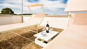 En takterrass med en solstol, ett bord med en vinflaska, två glas och en skål.
