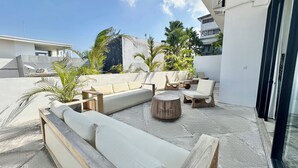 A rooftop terrace with a sofa, chairs, and a round table, surrounded by potted plants and a clear sky. - Spacious 7-bedroom villa in Canggu: Private chef, Pool, Movie theater (Badung)
