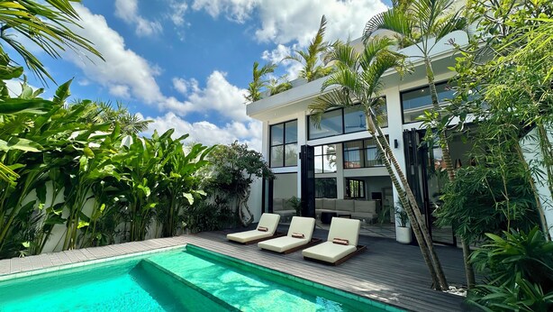 A modern house with a pool, lounge chairs, and lush greenery. - Spacious 7-bedroom villa in Canggu: Private chef, Pool, Movie theater (Badung)