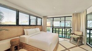 A modern hotel room with a large bed, a wooden nightstand, a seating area with a chair, and a balcony with a view of the city. - Spacious 7-bedroom villa in Canggu: Private chef, Pool, Movie theater (Badung)