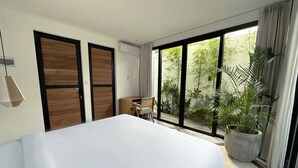 A bedroom with a large bed, a desk, and a view of a garden through large sliding doors. - Spacious 7-bedroom villa in Canggu: Private chef, Pool, Movie theater (Badung)