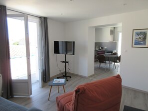 A living room with a sofa, a TV on a stand, a dining area with a table and chairs, and a kitchen in the background. - 3-room apartment ideally located (Fouras)