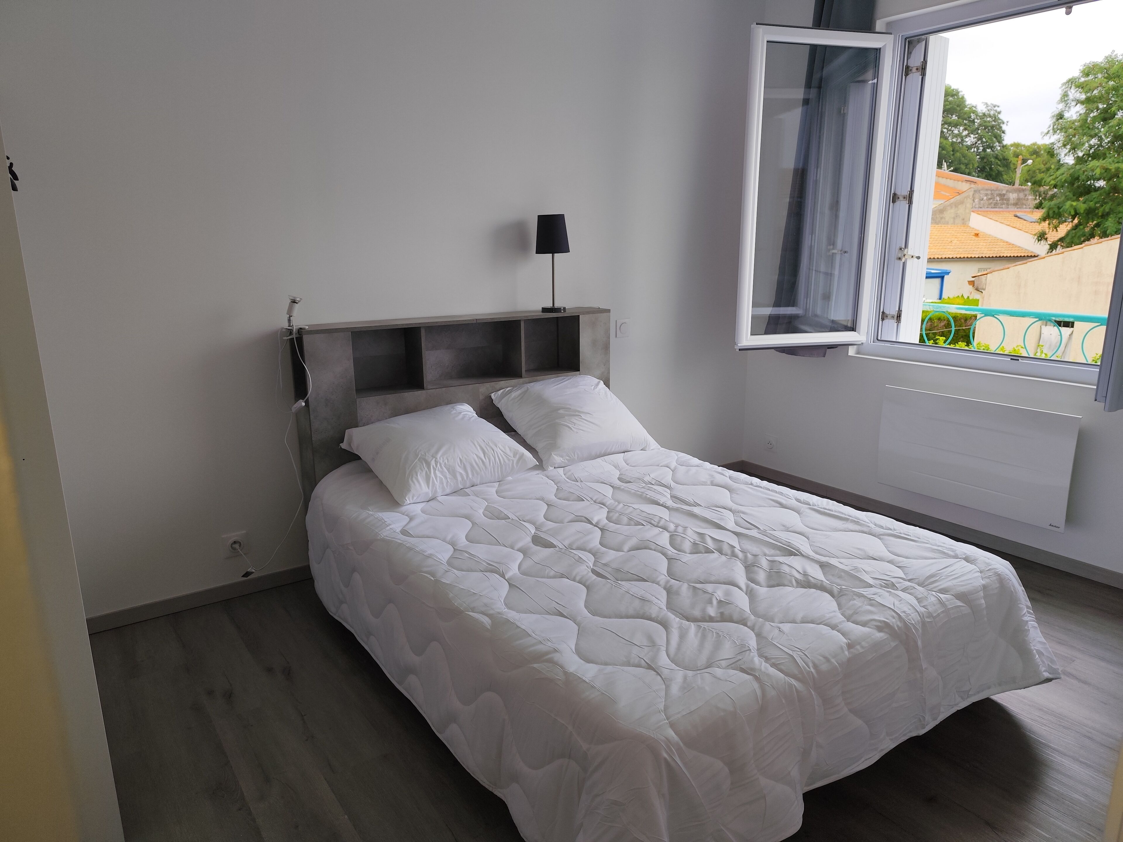 A bedroom with a bed, a bedside lamp, a window with curtains, and a view of the outside.