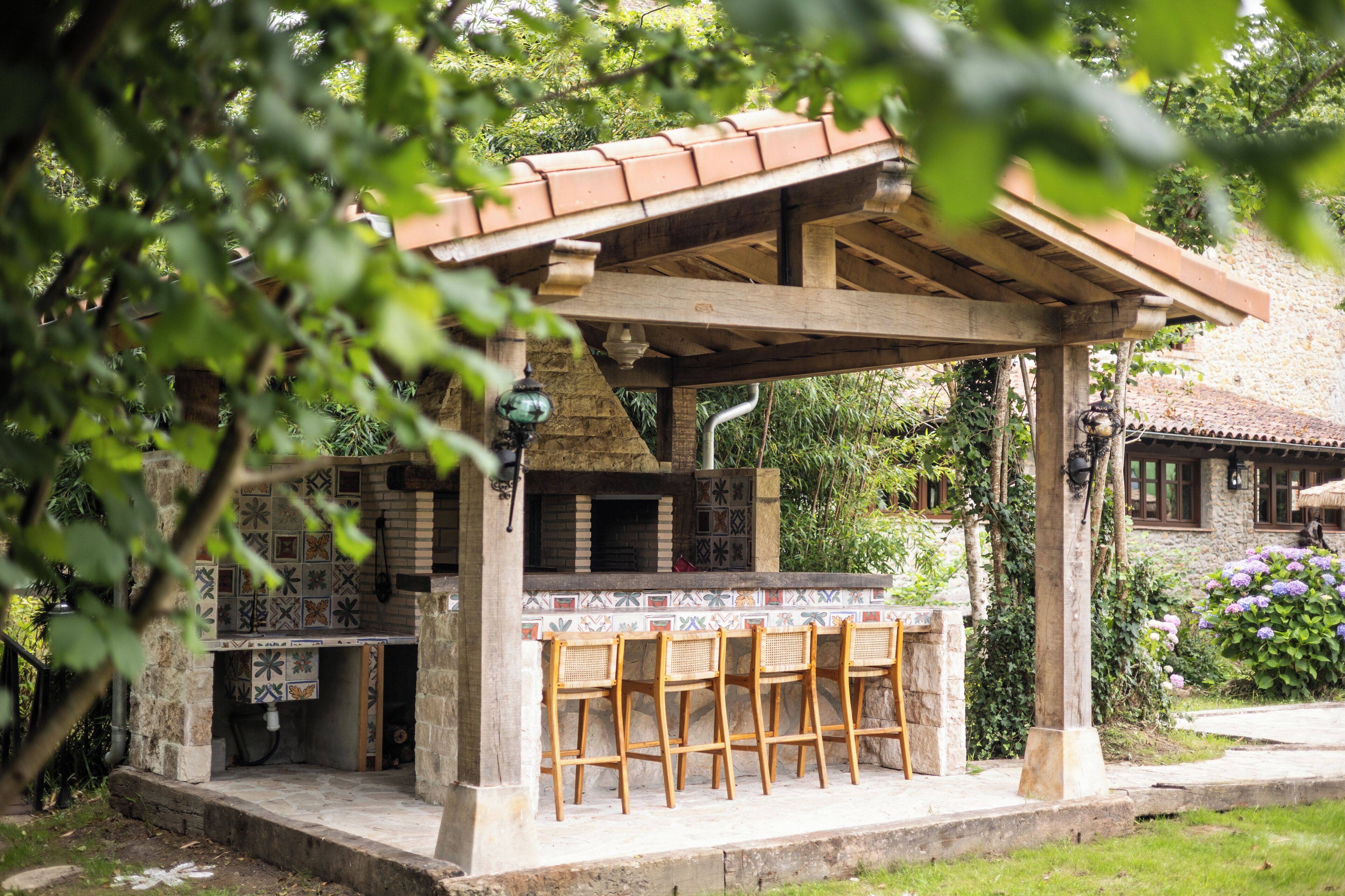 An outdoor patio with a tiled backsplash, wooden chairs, and a pergola structure.