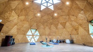Une grande pièce en forme d’étoile, avec un plafond en bois et une lucarne, un plancher en bois et divers objets, comme une guitare et des poteries.