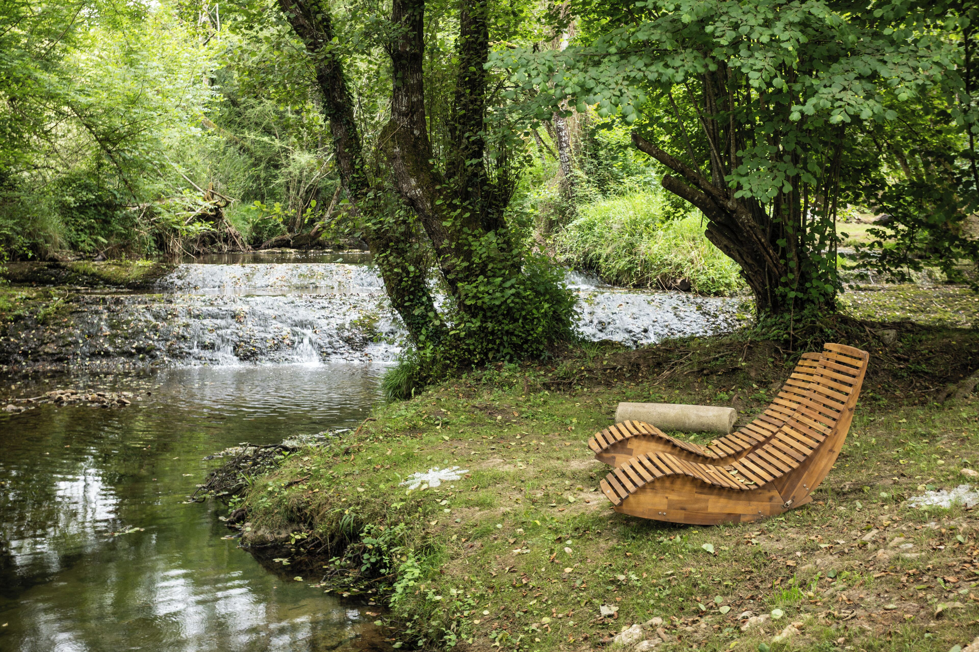A wooden bench by a river in a forested area.