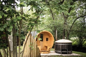 Una cabaña de madera con entrada circular, una sauna independiente y una terraza de madera.