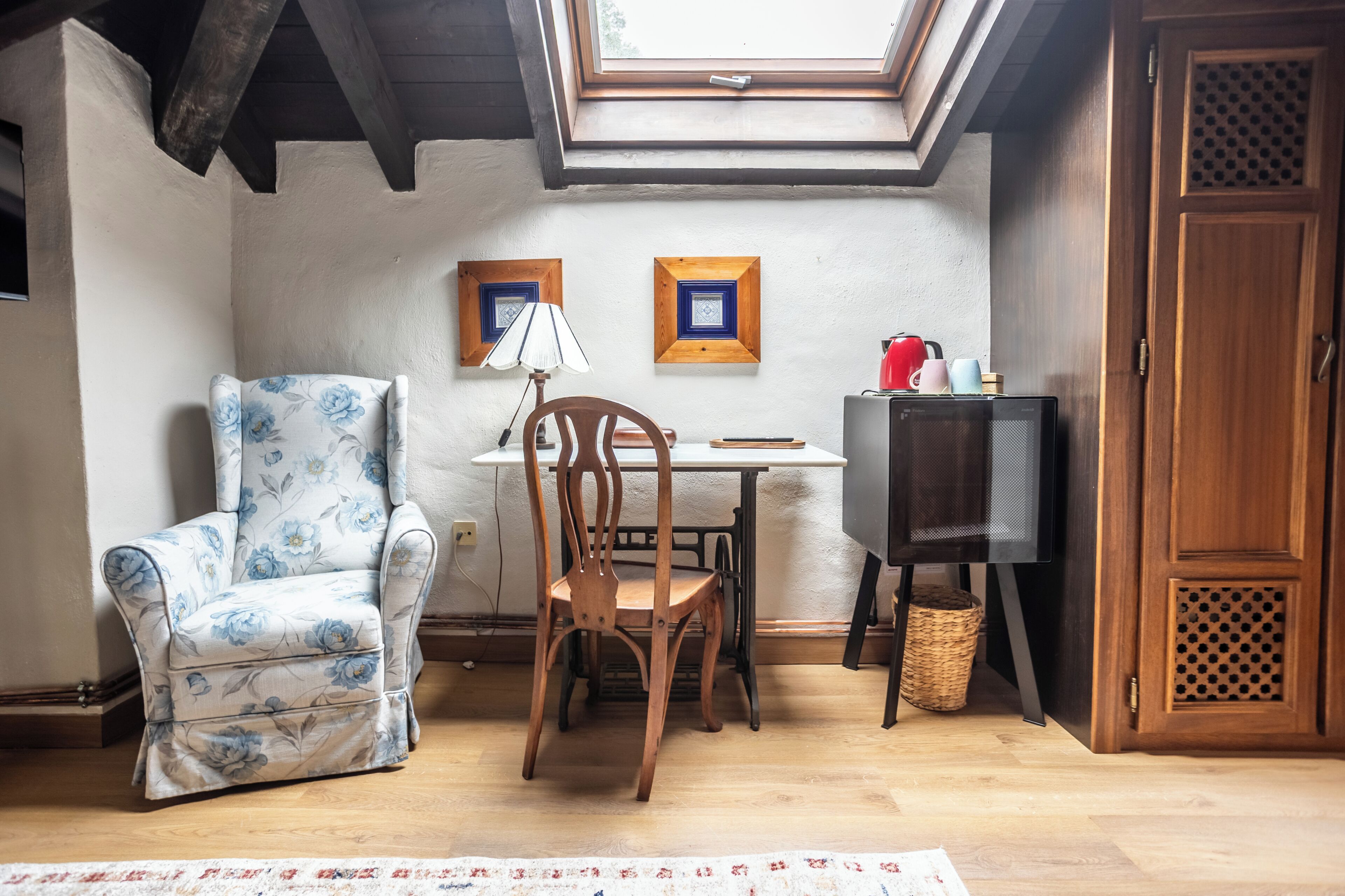 A cozy room with a skylight, a wooden chair, a table with a lamp, and a television.