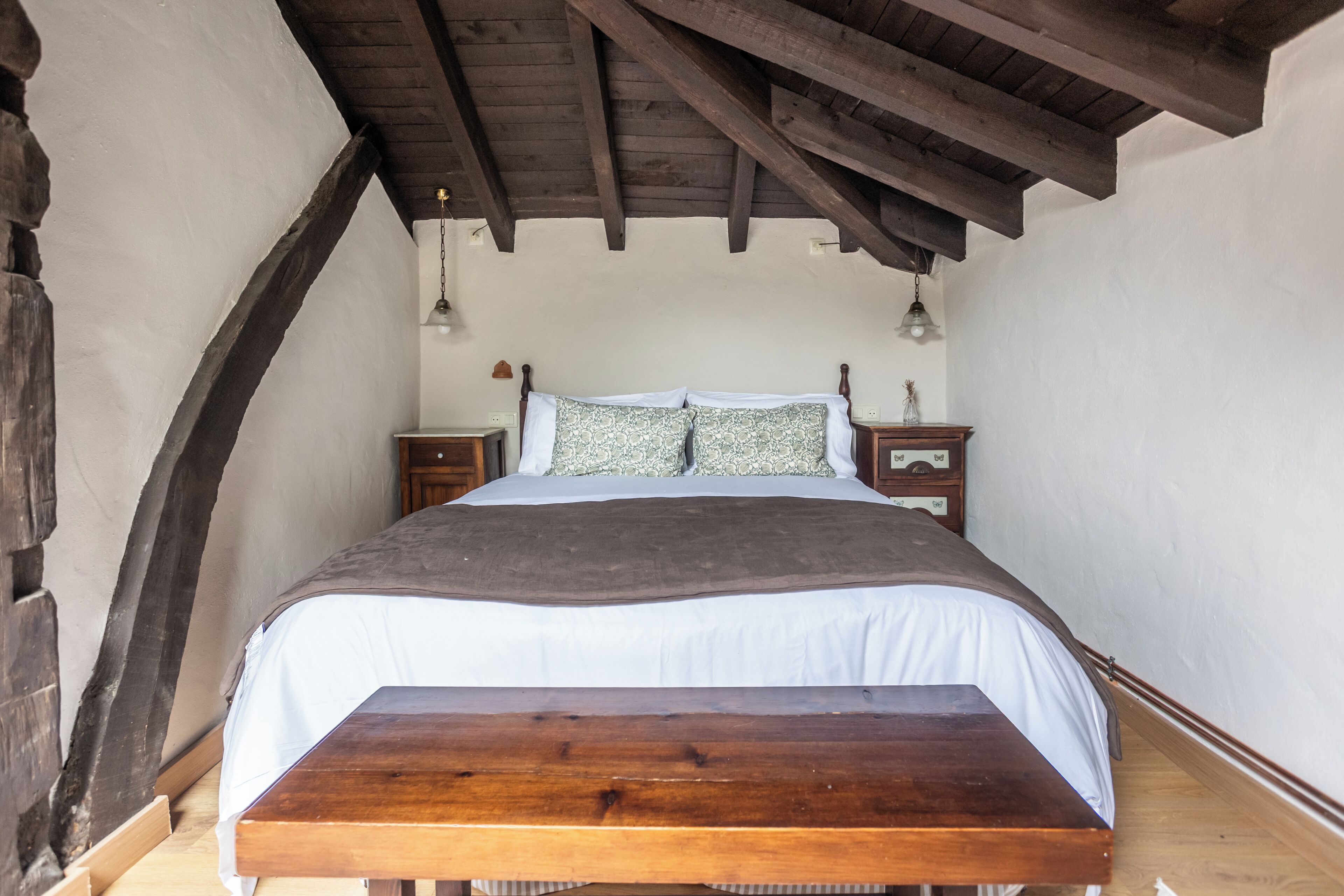 Un dormitorio con cama de madera, ropa de cama blanca, una mesita de noche y una lámpara colgante.