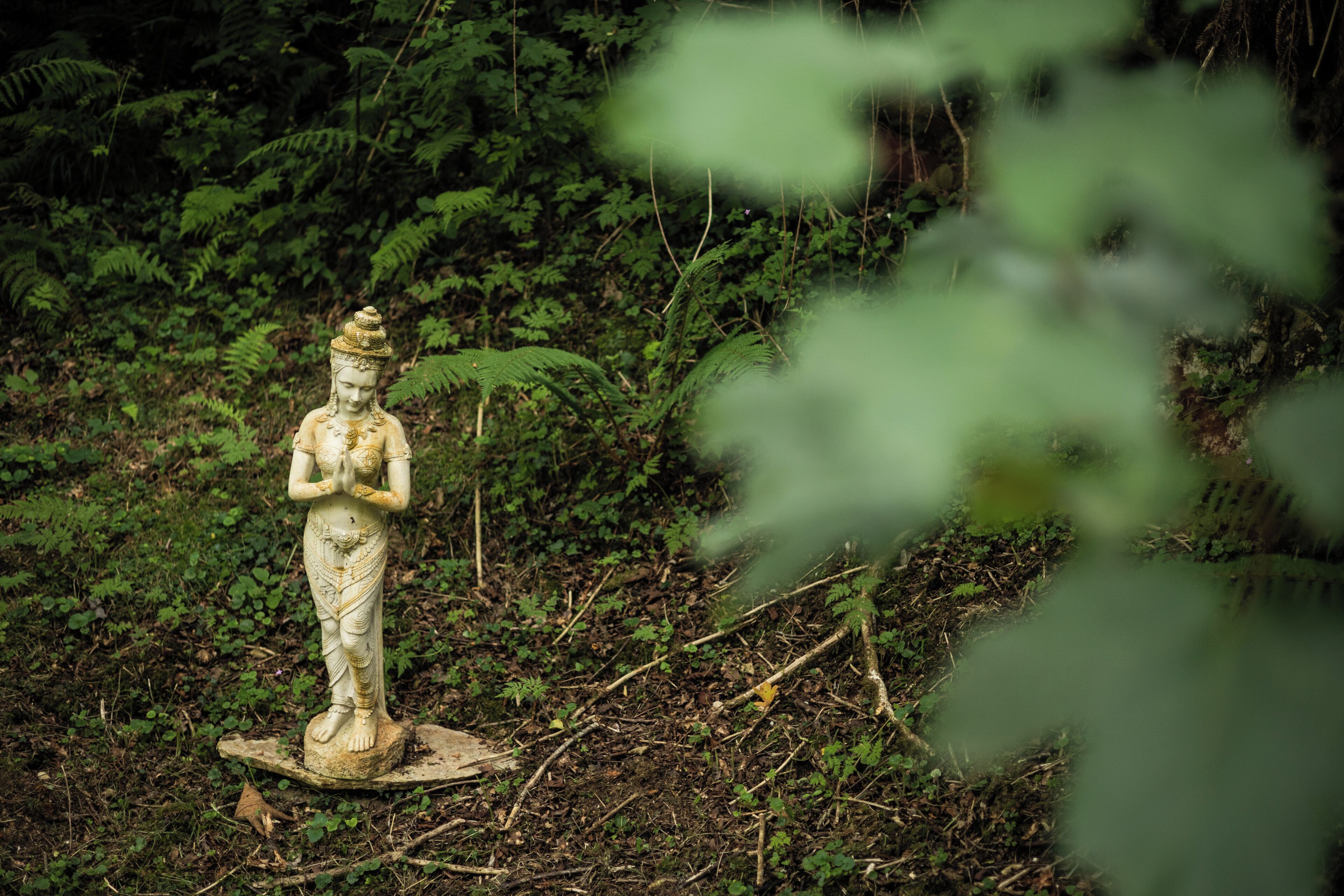 En statue i et naturligt landskab med frodig vegetation i baggrunden.