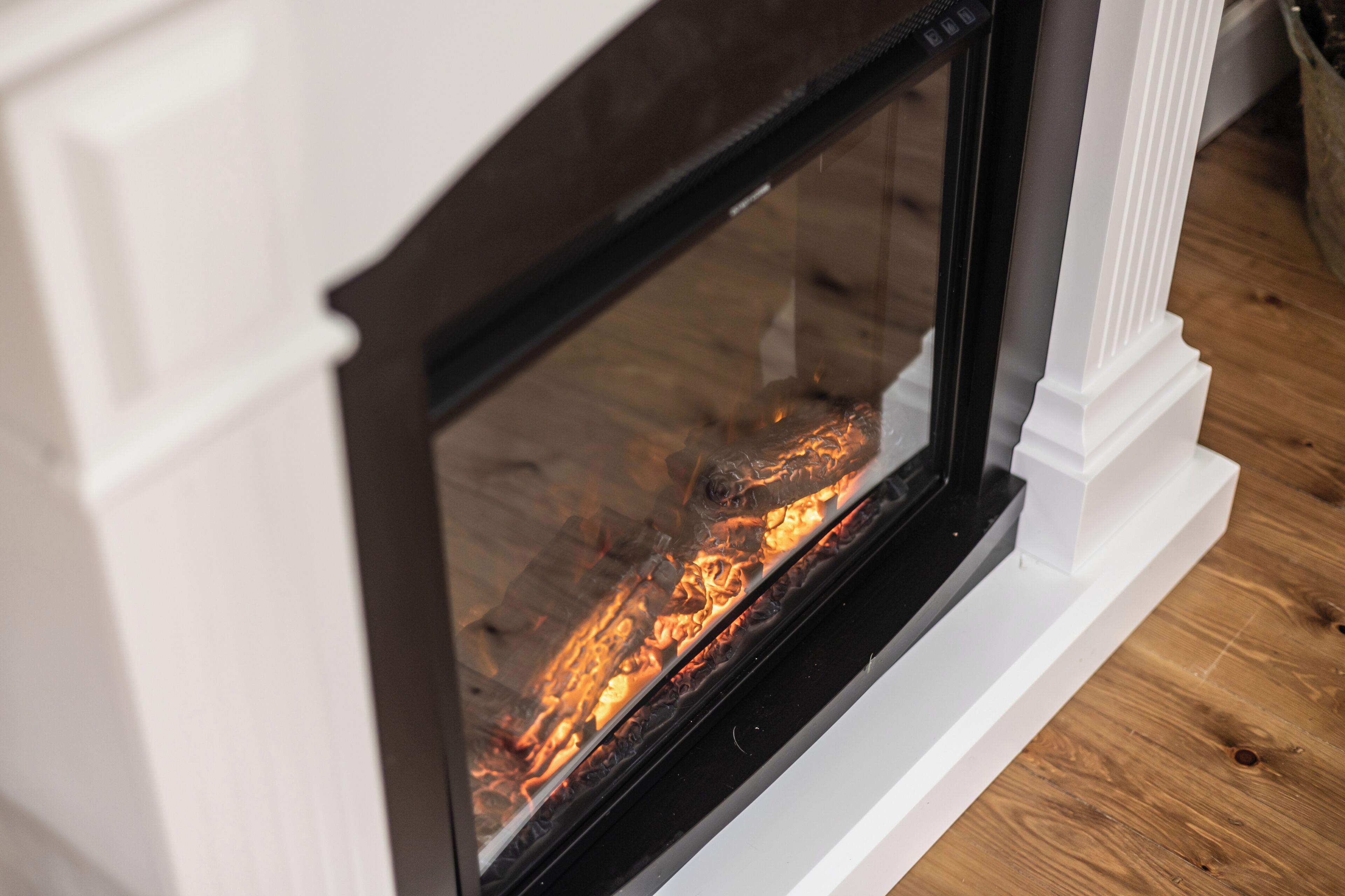 A fireplace with a visible fire, white mantel, and wooden floor.