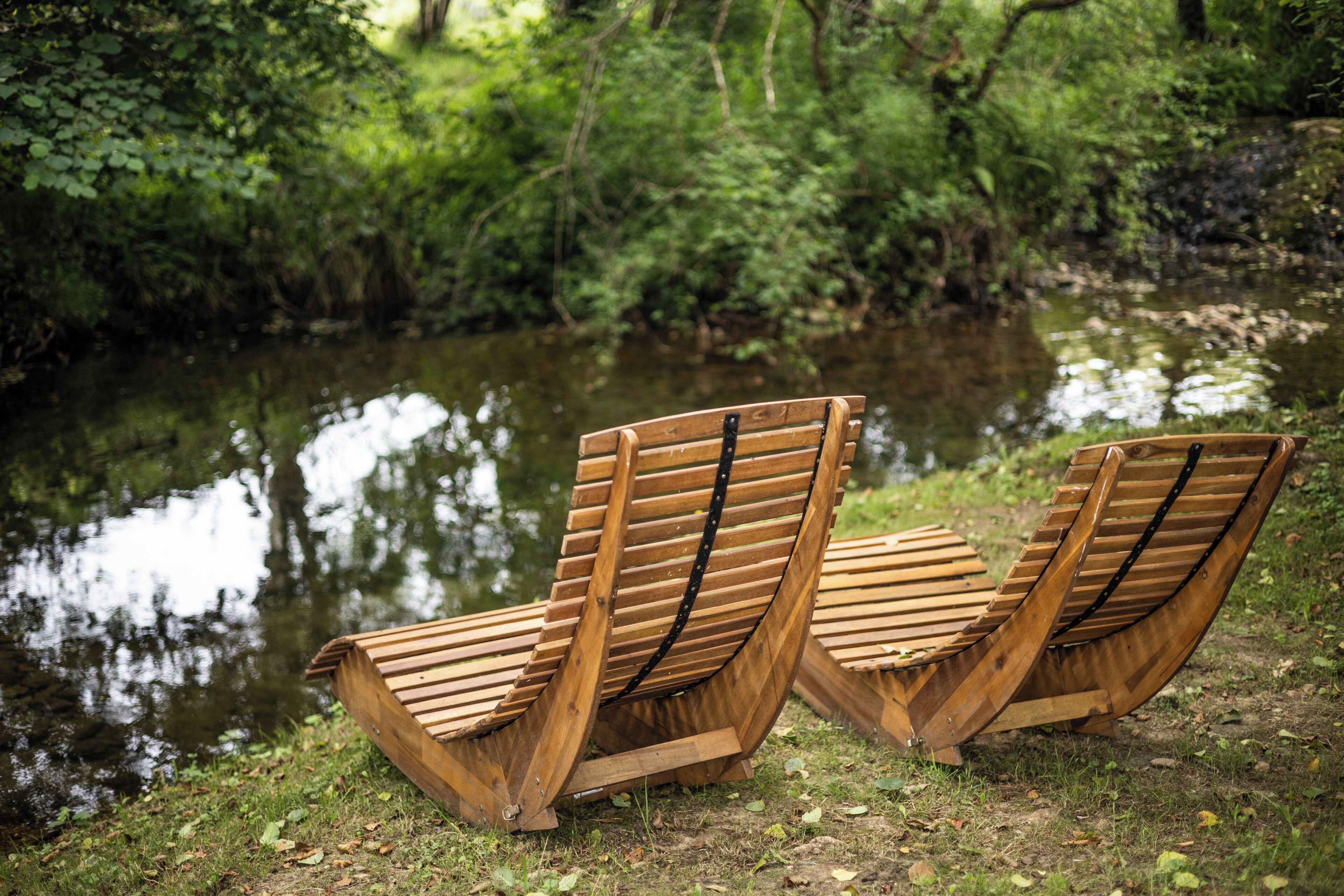 Tres sillones de madera junto a un río tranquilo en un área boscosa.