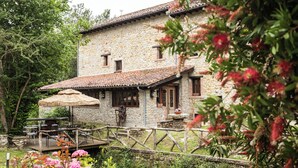 Un bâtiment en pierre doté d’une terrasse en bois, d’un parasol en chaume et d’une clôture rustique.