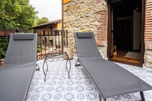 Dos tumbonas en un patio con diseño, junto a una pared de piedra y una puerta de madera al fondo.