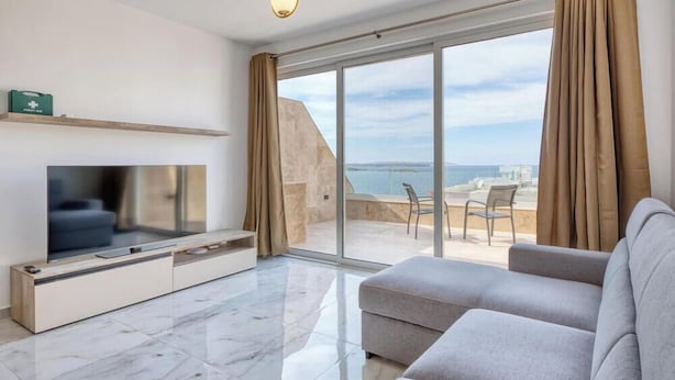 A modern living room with a flat-screen TV, a sofa, and a balcony with a view of the sea. - Penthouse Paradise in Qawra opposite the beach ! (St. Paul`s Bay)