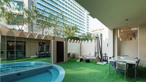 A modern hotel with a swimming pool, outdoor seating, and a view of a high-rise building.