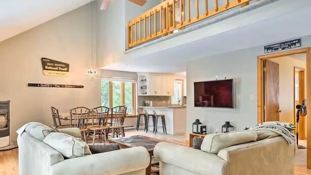 A spacious living room with a high ceiling, a dining area with wooden chairs, a kitchen with white cabinets, and a sign indicating a national forest.