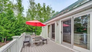 A covered deck with a table and chairs, a red umbrella, and a glass door leading to an outdoor area.