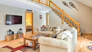 A living room with a sofa, coffee table, and a TV. There's a staircase with a wooden railing leading to an upper level.