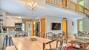 A spacious living area with a wooden dining table, chairs, and a staircase.