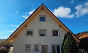 Ein zweistöckiges Haus mit Satteldach, zahlreichen Fenstern und einer sichtbaren Tür.