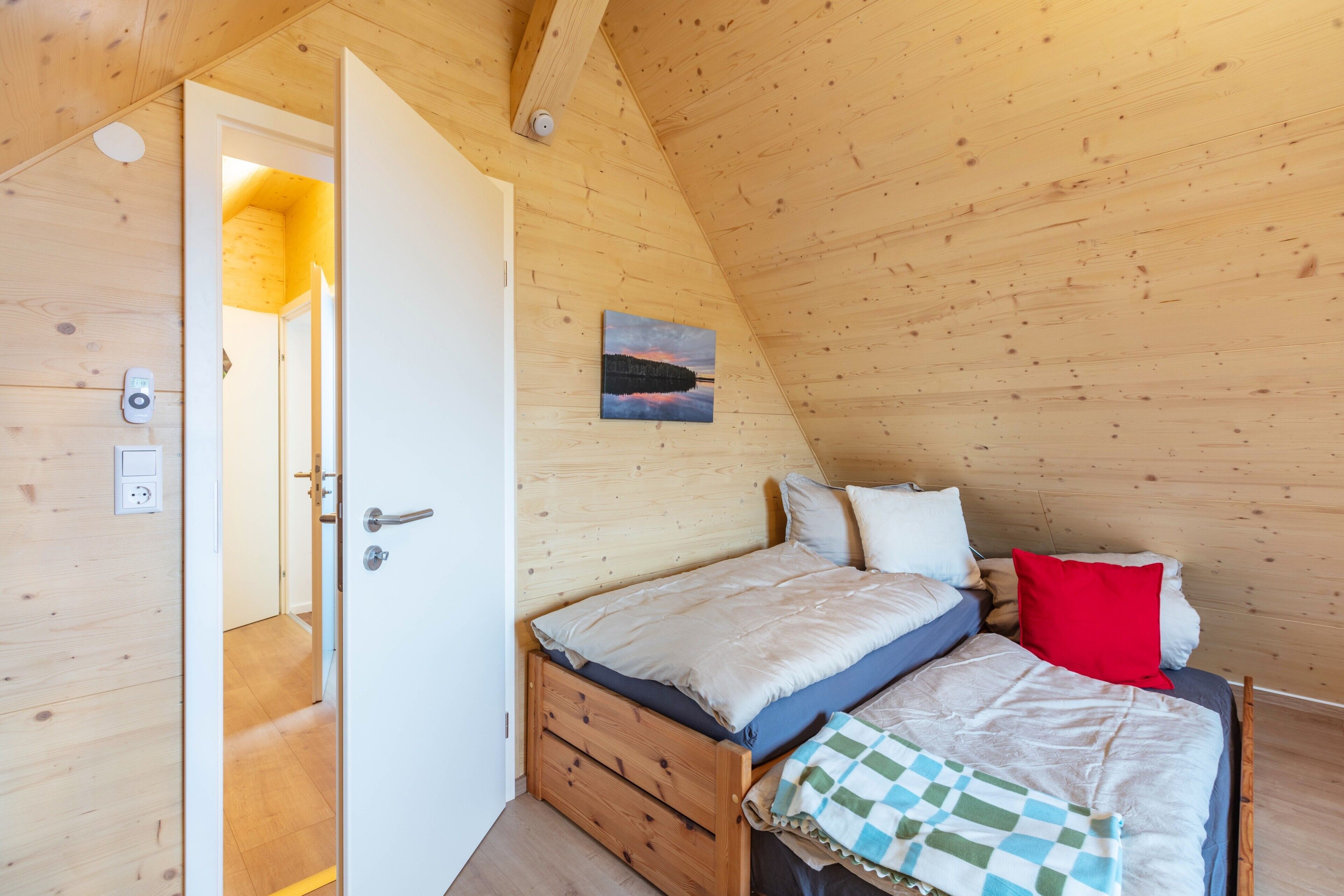 Une chambre aux murs lambrés, avec un lit, une porte et un thermostat fixé au mur.