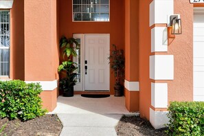 A house with a white door, potted plants, and a light fixture on the wall. - Family-Friendly 6BR Villa w/ Pool, Game Room (Kissimmee)
