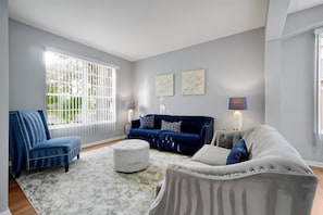 A living room with a blue armchair, a blue sofa, a white sofa, a round ottoman, and two wall-mounted lamps. - Family-Friendly 6BR Villa w/ Pool, Game Room (Kissimmee)