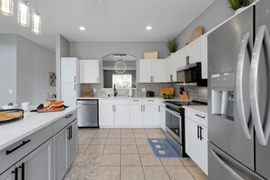 A modern kitchen with white cabinets, stainless steel appliances, and a herringbone tile floor. - Family-Friendly 6BR Villa w/ Pool, Game Room (Kissimmee)