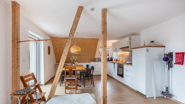 Een moderne keuken met houten balken, een eethoek met stoelen en een witte koelkast.