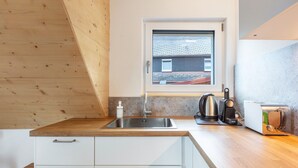 Een moderne keuken met een houten aanrecht, een roestvrijstalen spoelbak en een raam met uitzicht op een gebouw, en een broodrooster op het aanrecht.