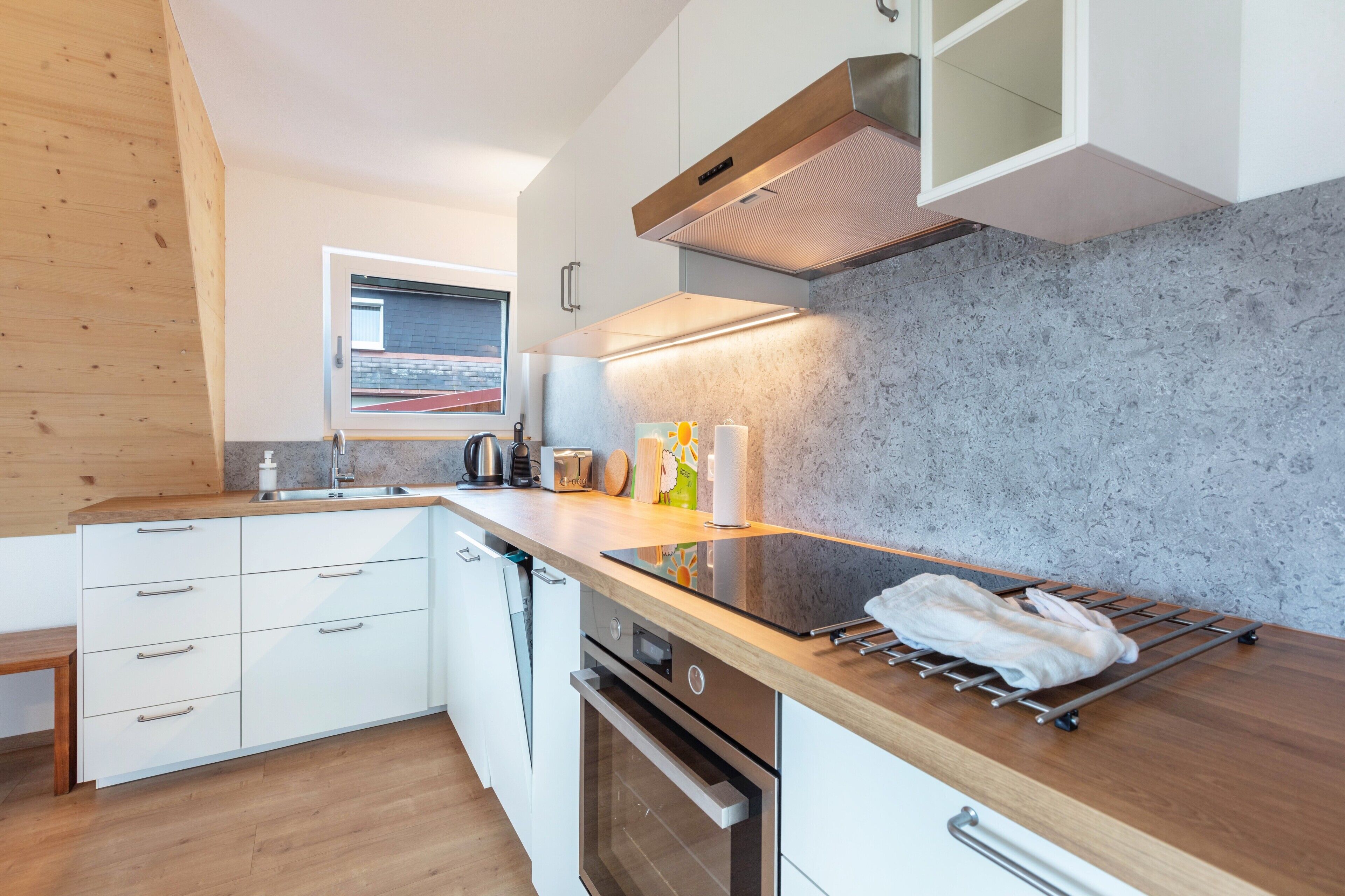 Une cuisine moderne avec des armoires blanches, une hotte de cuisinière en acier inoxydable et un plan de travail en bois.