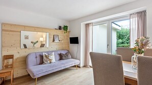 Een moderne woonkamer met een bank, een houten accentmuur, een flatscreen televisie en een eethoek met stoelen en een tafel.